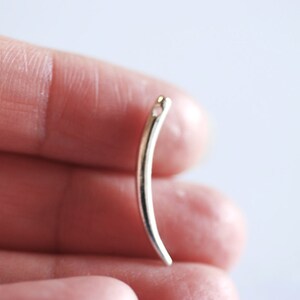 Op de afbeelding: Een zilverkleurige metalen naaldendraaier met een gebogen vorm en een klein gaatje bovenaan.