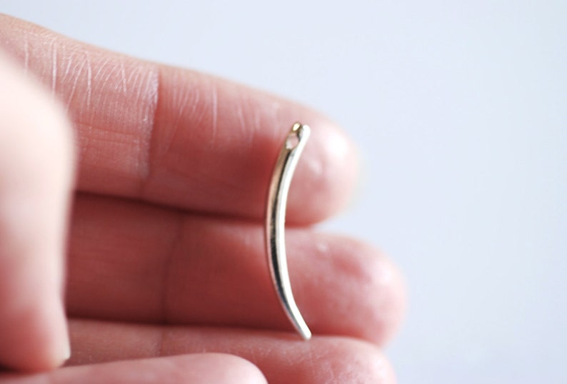 Op de afbeelding: Een zilverkleurige metalen naaldendraaier met een gebogen vorm en een klein gaatje bovenaan.