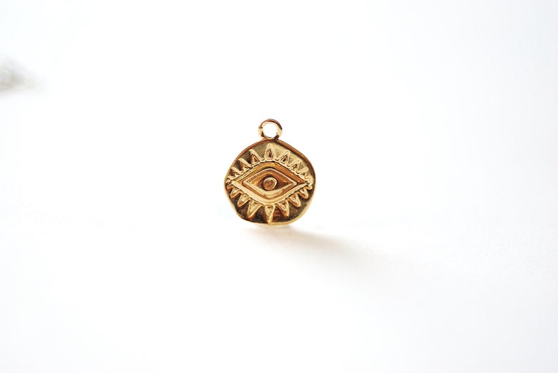 Puede incluir: Encanto dorado con un dise&ntilde;o de ojo detallado, rodeado de un patr&oacute;n de estrella. El encanto es un s&iacute;mbolo popular de protecci&oacute;n y buena suerte.