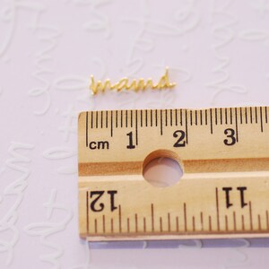 May include: A gold-colored metal word charm that reads "brand" is placed on a wooden ruler with centimeter markings. The ruler is marked from 1 to 5 centimeters.