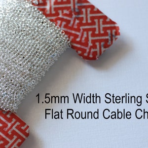 May include: A close-up of a silver flat round cable chain, 1.5mm wide. The chain is coiled and wrapped in red and white patterned fabric.