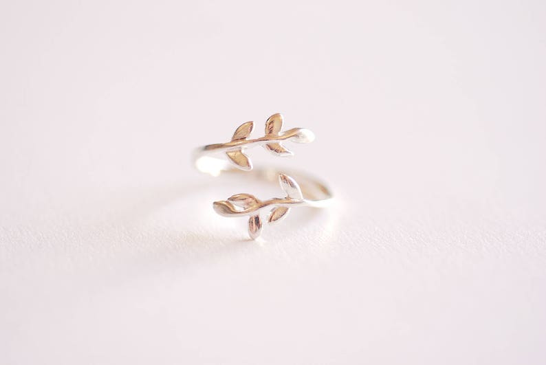 May include: A silver ring with a delicate design of two intertwined branches with leaves.
