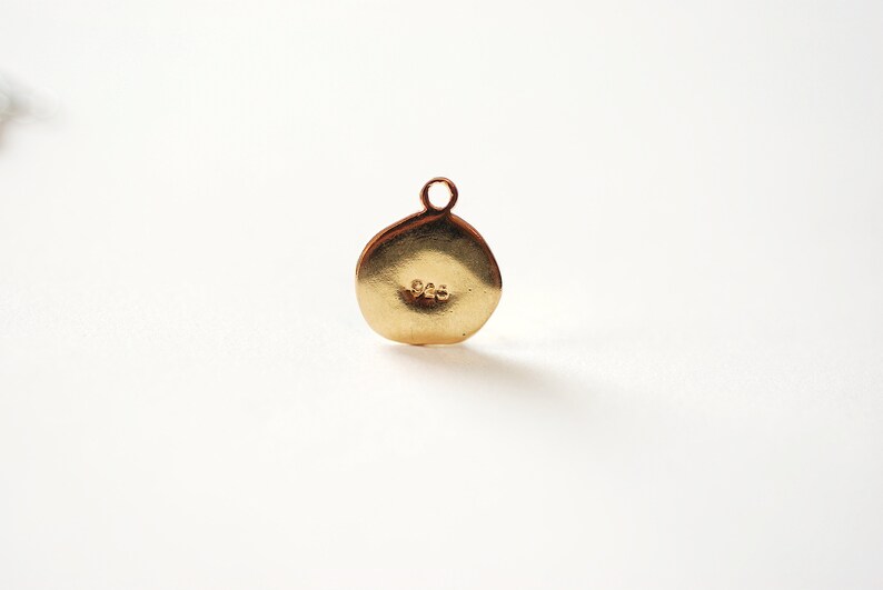 Puede incluir: Un charm redondo de color dorado con un bucle en la parte superior. El charm tiene el n&uacute;mero "925" estampado en la parte posterior.