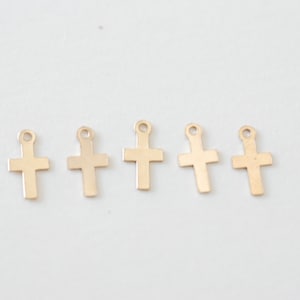 May include: Five gold-colored metal cross charms with a loop at the top for attaching to jewelry or other crafts.