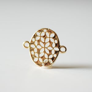 May include: Gold-toned metal connector with a circular, openwork design featuring a repeating floral pattern. The connector has two small loops on either side.