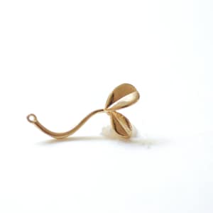 May include: A gold-colored metal charm shaped like a four-leaf clover with a loop at the bottom for attaching to a necklace or bracelet.