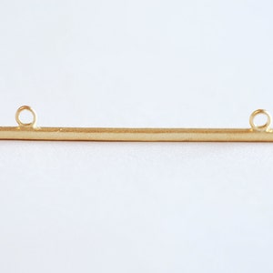 May include: Gold bar pendant with two jump rings. The bar is smooth and has a slightly textured finish.