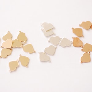 May include: A collection of heart-shaped metal charms in gold, silver, and rose gold finishes. The charms have two jump rings for attaching to jewelry or other crafts.