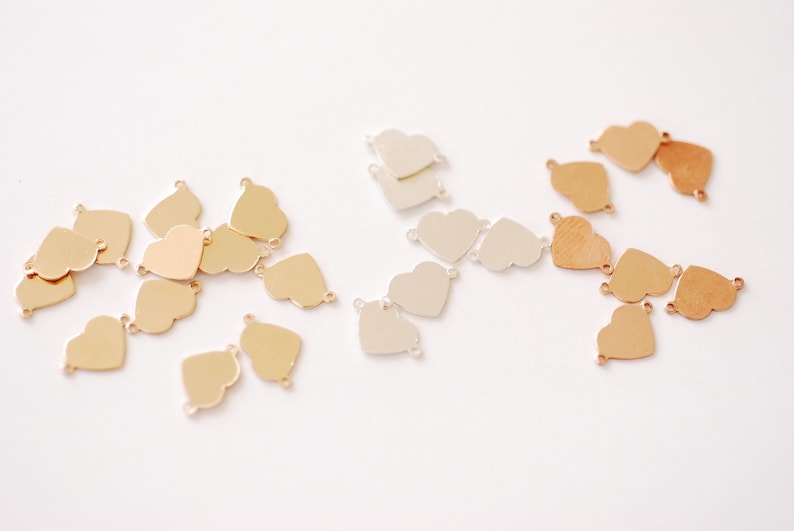May include: A collection of heart-shaped metal charms in gold, silver, and rose gold finishes. The charms have two jump rings for attaching to jewelry or other crafts.