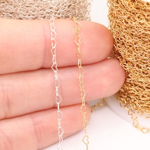 May include: Two spools of heart-shaped chain, one silver and one gold. The chain is shown draped over a hand.