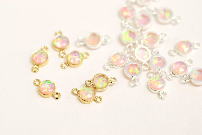 May include: A close-up of a variety of gold and silver connector charms with iridescent pink opal stones. The charms have two loops on each side, making them ideal for adding to necklaces, bracelets, or earrings.