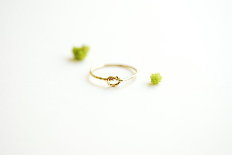 May include: A simple gold ring with a knot design. The ring is on a white background.