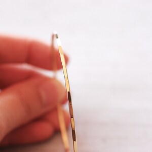 May include: A gold bangle bracelet with a hammered finish. The bracelet is thin and delicate, and it has a simple, elegant design.
