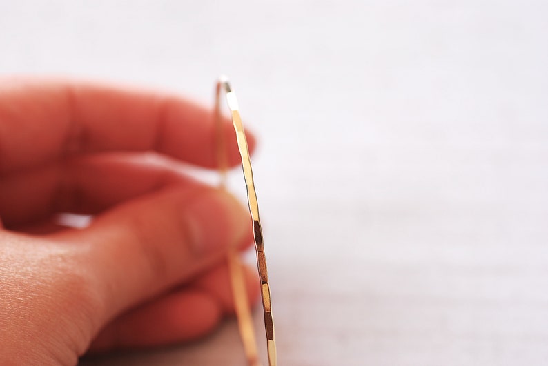 May include: A gold bangle bracelet with a hammered finish. The bracelet is thin and delicate, and it has a simple, elegant design.