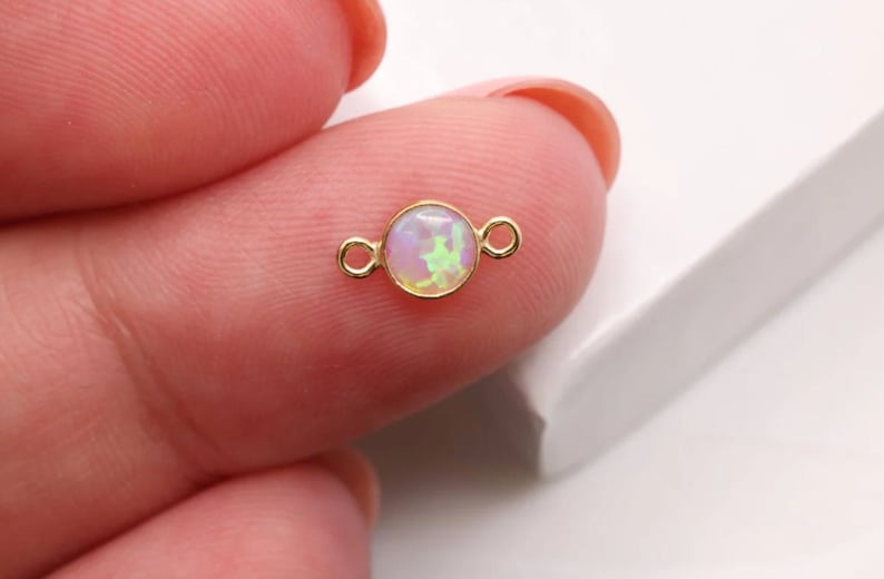 May include: Gold-toned connector with a round opal gemstone. The opal is iridescent with pink, white, and green hues.