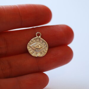 Puede incluir: Encanto de plata con un dise&ntilde;o de ojo detallado, rodeado de un c&iacute;rculo de puntos. El encanto es un s&iacute;mbolo popular de protecci&oacute;n y buena suerte.
