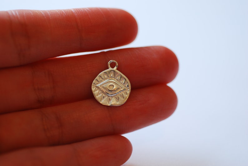 Puede incluir: Encanto de plata con un dise&ntilde;o de ojo detallado, rodeado de un c&iacute;rculo de puntos. El encanto es un s&iacute;mbolo popular de protecci&oacute;n y buena suerte.