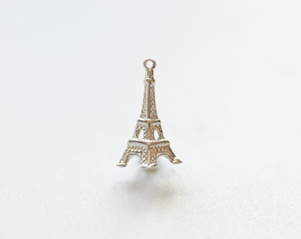 May include: Silver charm in the shape of the Eiffel Tower. The charm is detailed with intricate designs and has a loop at the top for attaching to a bracelet or necklace.