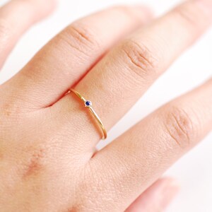 May include: A delicate gold ring with a single small blue gemstone.