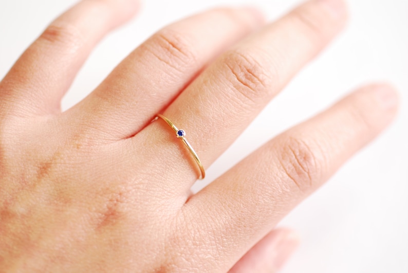 May include: A delicate gold ring with a single small blue gemstone.