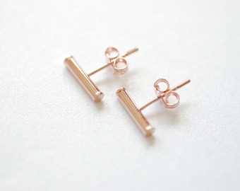 May include: A pair of rose gold bar stud earrings. The earrings are simple and minimalist, with a straight bar design.