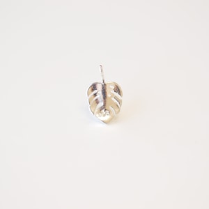 May include: Silver monstera leaf stud earring. The earring is a simple, minimalist design.