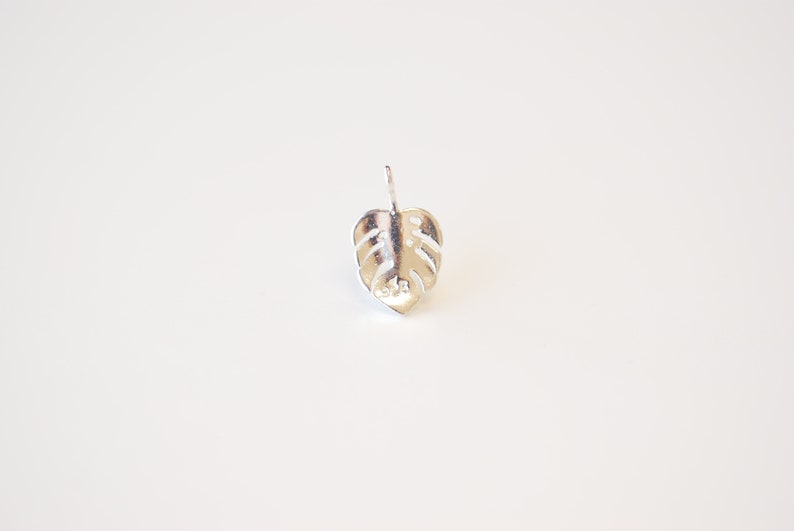 May include: Silver monstera leaf stud earring. The earring is a simple, minimalist design.