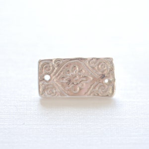 May include: A silver charm with a detailed embossed design, resembling a classic cookie.