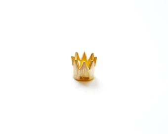 May include: A small gold crown charm with a textured surface. The crown has a pointed top and a rounded base. The charm is marked with the number "S795" on the bottom.