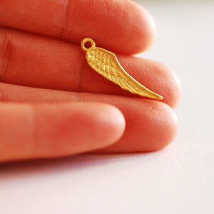 May include: A gold-colored metal wing charm pendant. The wing is detailed with a textured surface.