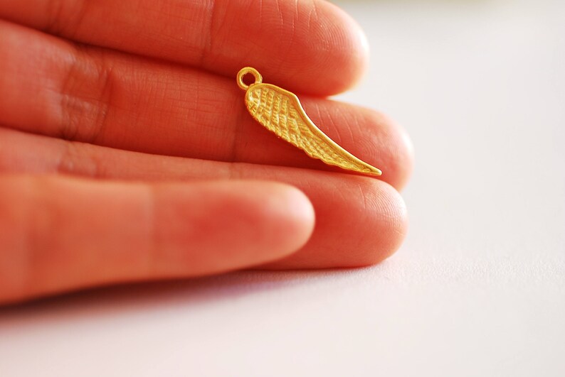 May include: A gold-colored metal wing charm pendant. The wing is detailed with a textured surface.