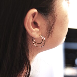 May include: A close-up of a person's ear with a pair of silver double hoop earrings. The earrings are simple and elegant.