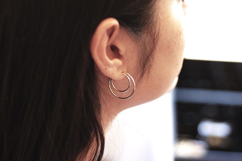 May include: A close-up of a person's ear with a pair of silver double hoop earrings. The earrings are simple and elegant.