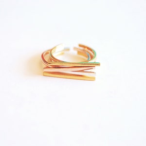 May include: Set of four gold-toned stacking rings. The rings are made of thin metal and have a simple, minimalist design.