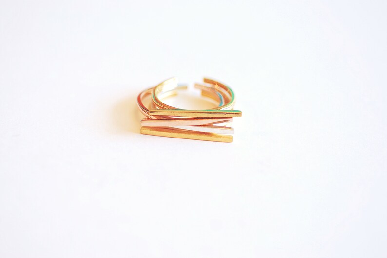 May include: Set of four gold-toned stacking rings. The rings are made of thin metal and have a simple, minimalist design.