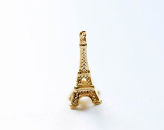 May include: A gold-colored Eiffel Tower charm pendant. The charm is detailed with intricate designs and has a loop at the top for attaching to a necklace or bracelet.