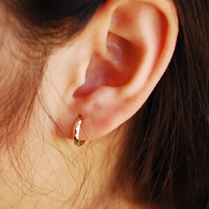 May include: A close-up of a person's ear with a gold hoop earring. The earring is hammered and has a textured surface.