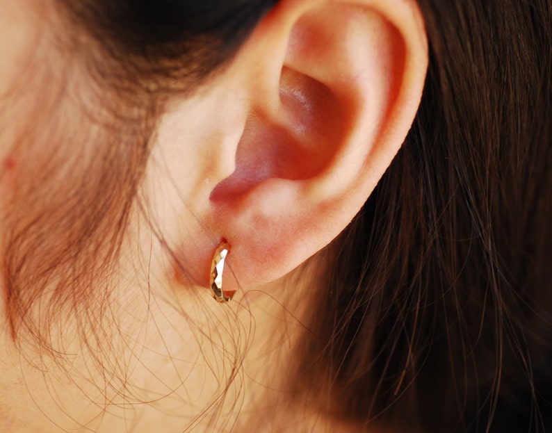 May include: A close-up of a person's ear with a gold hoop earring. The earring is hammered and has a textured surface.