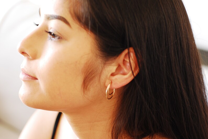 May include: A close-up of a woman's face, showing her profile. She has long, dark brown hair and is wearing a pair of gold hoop earrings.