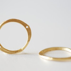 May include: Two gold-toned metal rings with a slightly irregular, organic shape. The rings have small holes on the sides.