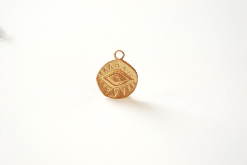 Puede incluir: Encanto dorado con un dise&ntilde;o detallado de ojo turco con un patr&oacute;n de rayos de sol alrededor. El encanto es redondo y tiene un bucle en la parte superior para sujetarlo a un collar o pulsera.