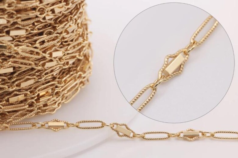 May include: Gold chain with a delicate, intricate design. The chain features oval links with a textured surface and rectangular accents.