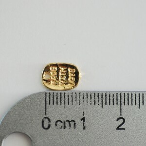 May include: Gold-coloured metal tag with the words "Made with Love" engraved on it. The tag is approximately 1 cm long and is next to a ruler.