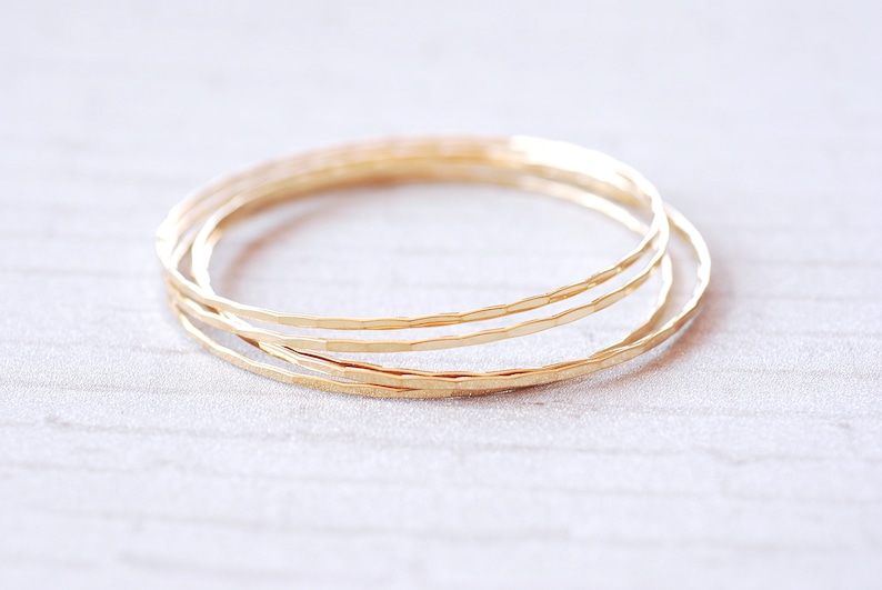May include: Set of three gold-toned hammered metal bangles. The bangles are stacked on top of each other.