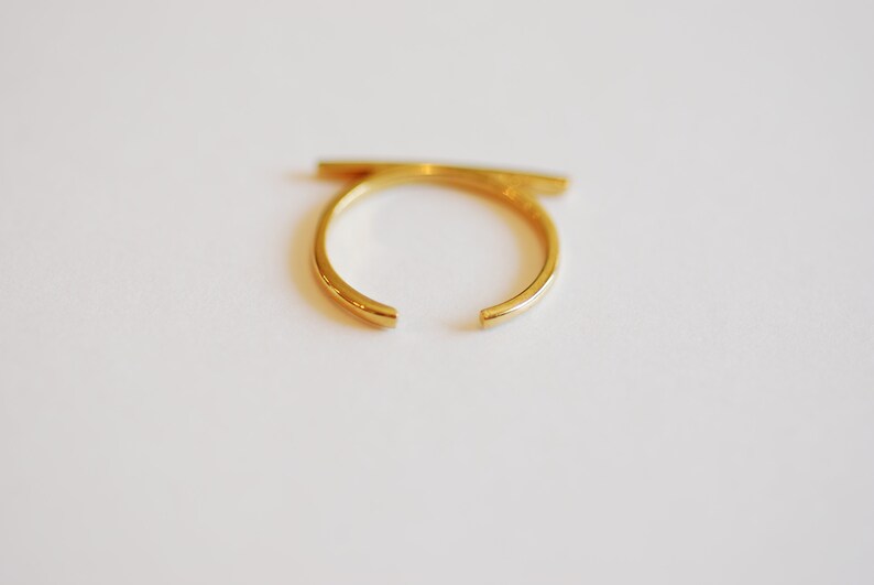 May include: A gold-colored ring with a horizontal bar across the top.