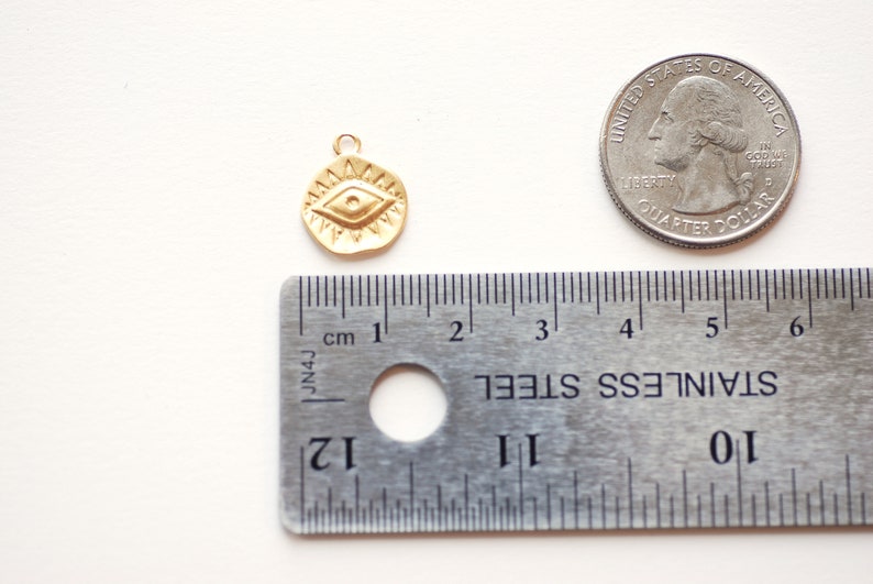 Puede incluir: Encanto dorado con un dise&ntilde;o de ojo detallado, que mide aproximadamente 1 cm de di&aacute;metro. El encanto se muestra junto a una moneda de 25 centavos de d&oacute;lar estadounidense para comparar el tama&ntilde;o.