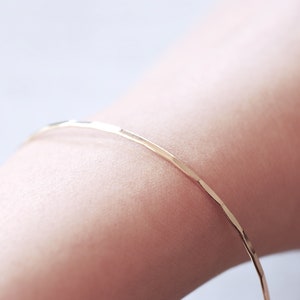 May include: A thin gold bangle bracelet with a hammered texture.