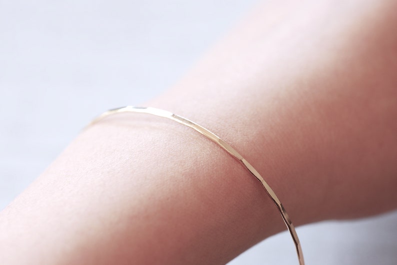 May include: A thin gold bangle bracelet with a hammered texture.