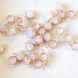 May include: A collection of gold-toned metal connector charms with iridescent pink opal-like stones. Each charm has two loops for attaching to jewelry.