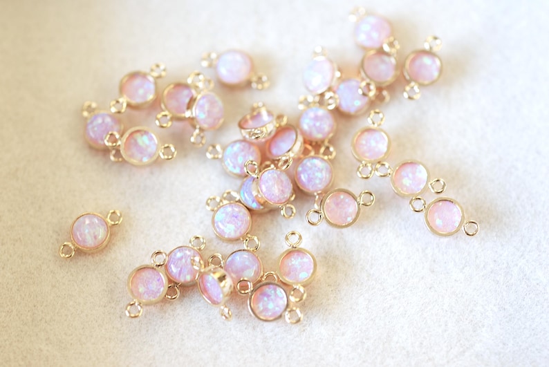 May include: A collection of gold-toned metal connector charms with iridescent pink opal-like stones. Each charm has two loops for attaching to jewelry.